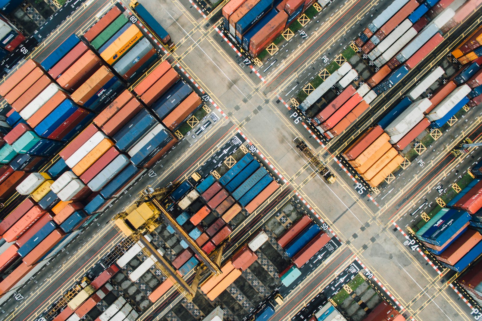 Aerial top-down view of colourful shipping containers stacked in a port yard — illustrating how import order volume, not just unit price, drives landed cost per unit.